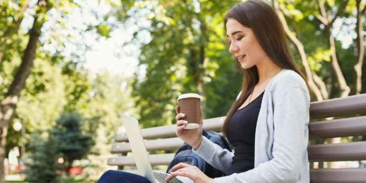 Mujer con portatil tomando un café en el parque