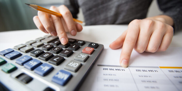 Closeup of accountant counting on calculator and working with table